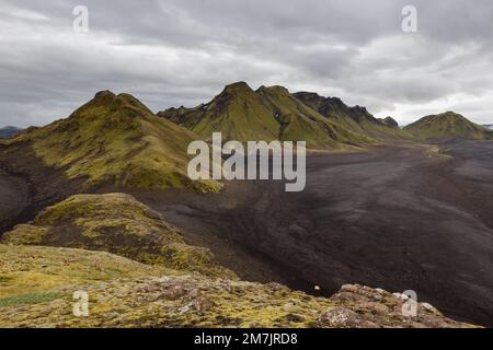 Paesaggio malinconico dell'Islanda con un deserto di lava nera senza fine e montagne verdi ricoperte di folta muschio islandese. Foto Stock