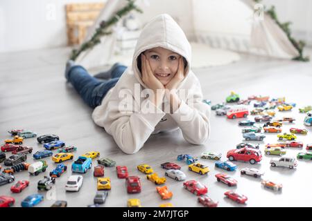 Carino bambino preteen, ragazzo dolce, giocando con le auto di coloful, dimensioni e colori diversi sul pavimento in felpa con cappuccio Foto Stock