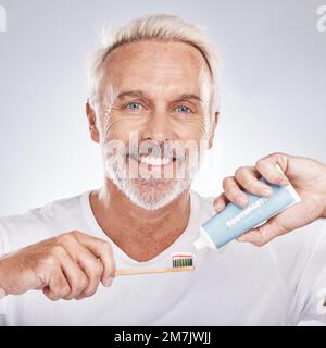 Spazzolino da denti, viso e uomo anziano con dentifricio in studio su sfondo grigio. Ritratto, pulizia e vecchio modello maschile tenendo prodotto per spazzolatura Foto Stock