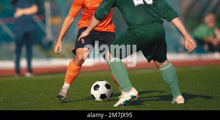 Due giocatori di calcio adulti che calcia la palla di calcio in un duello. Gara di calcio tra due squadre. Giocatori anonimi che corrono e calci palla Foto Stock
