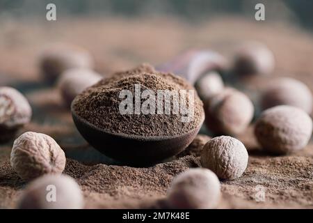 Noce moscata essiccata in un cucchiaio di legno con noce moscata intera nelle vicinanze. Messa a fuoco selettiva con primo piano e sfondo sfocati. Foto Stock