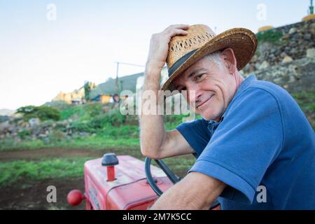 Un contadino sorridente tiene il cappello da cowboy mentre si siede sul trattore. Foto Stock