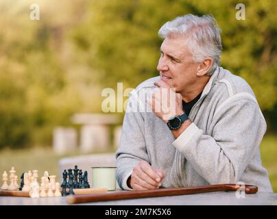 Uomo anziano, parco e pensiero per gli scacchi, gioco e concorrenza a tavola da alberi, sole e fuoco. Gioco da tavolo per anziani, outdoor e strategia per Foto Stock