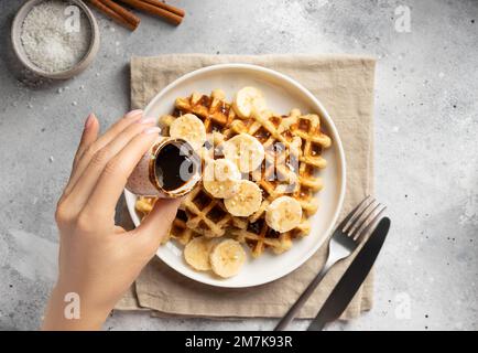 la mano della donna versa lo sciroppo di datteri sui cialde dell'avena della banana Foto Stock