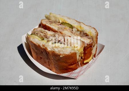 Un delizioso panino cubano con maiale tirato, sottaceti, formaggio e salsa su un piatto di carta. Cibo di strada autentico da un camion alimentare. Foto Stock