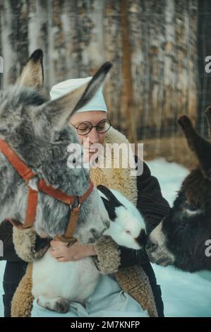 Veterinario medico premuroso tiene un coniglio in braccio e un asino accanto a lui. Il veterinario esamina gli animali Foto Stock