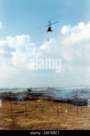 DF-SD-03-17786. [Completa] Didascalia scena: Un Kaman HH-43F Huskie (Pedro) abbassa AIRMAN di prima classe (A1C) William Hart Pitsenbarger, USAF, Paraseascue Crew Member, distaccamento 6, 38th Aerospace Rescue and Recovery Squadron (ARRS) in un minefield in fiamme presso la base aerea di Bien-Hoa nella Repubblica del Vietnam (RVN) per l'estrazione di un elicottero ferito soldato vietnamita. Il soldato ha perso un piede quando ha fatto un passo su una mina. Nessuno riusciva a capire come estrarre il soldato ferito senza inciampare sulle mine. A1c Pitsenbarger disse: "No problema, abbassami sul penetratore, e ti cavalcò la g Foto Stock