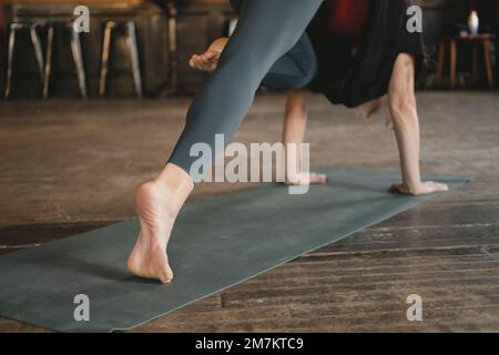 Donna irriconoscibile yoga nuovo insegnante facendo un cane a tre zampe rivolto verso il basso posa ginocchio a naso, allenamento yoga, a piedi nudi e indossare sportswe Foto Stock