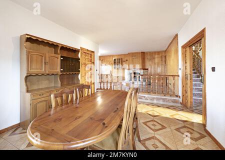 Sala da pranzo di una casa bassa con tavolo in legno di pino, mobili in noce, ringhiera in soggiorno a doppia altezza e camino con parete rivestita di vernice Foto Stock