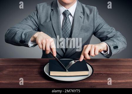 Un uomo d'affari con una forchetta e un coltello mangia un libro su un piatto Foto Stock