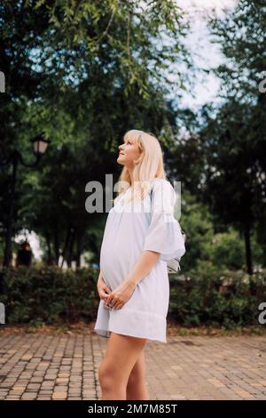 Donna incinta felice in vestito blu in giardino nei giorni estivi Foto Stock