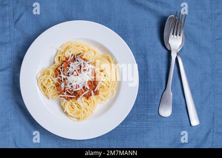 Spaghetti alla bolognese con parmigiano sul piatto bianco. Semplice sfondo blu e decorazione. Piatti tradizionali italiani, cucina mediterranea Foto Stock