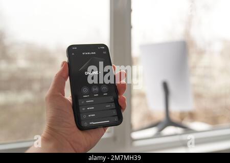 KIEV, UCRAINA - 8 GENNAIO 2023: Persona che utilizza l'app Starlink sullo smartphone, vista ravvicinata con l'antenna per ricevere il segnale in background. Foto Stock