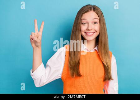 Ritratto foto di giovane allegro soddisfatto cute sorridente ragazza marrone capelli mostrando segno v indossare uniforme elegante isolato su sfondo di colore blu Foto Stock