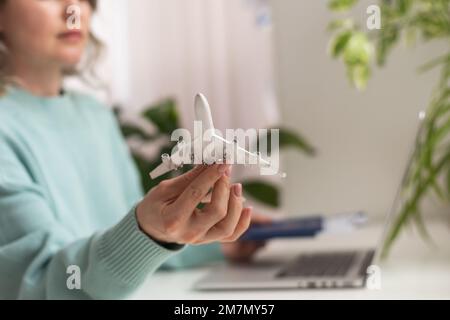 Positiva donna felice in vacanza estiva, seduta in ufficio con aereo giocattolo e mostrando passaporto, videochiamata Foto Stock