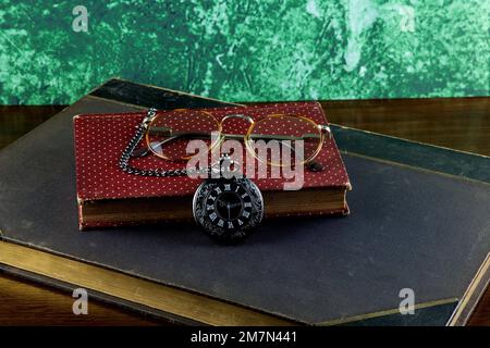 Orologio tascabile con vecchi libri e occhiali su una superficie di legno lucidato Foto Stock