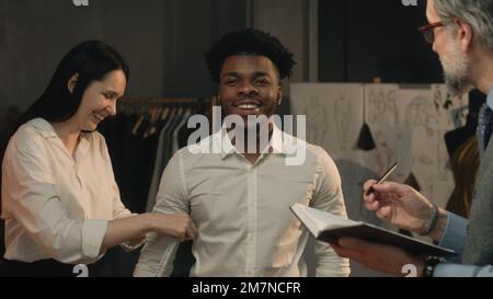 Scatto cinematografico di sartoria che prende le misure dell'uomo afroamericano per la camicia del vestito di affari o di nozze. Lussuoso atelier o studio su misura. Concetto di moda, fatto a mano e couturier. Foto Stock