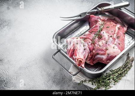 Agnello di montone marinato a spalla intera, carne cruda in un vassoio di acciaio con erbe e spezie. Sfondo bianco. Vista dall'alto. Spazio di copia. Foto Stock