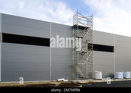 Facciata grigia a pannelli sandwich di un magazzino non finito, impalcatura tubolare multilivello, sfondo blu cielo Foto Stock