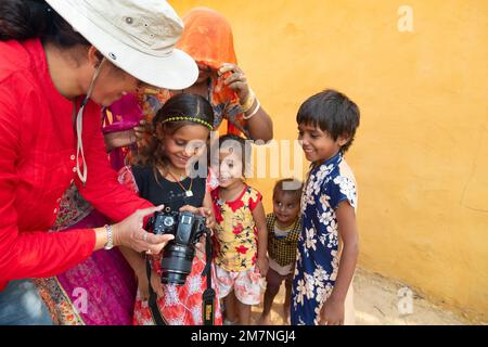 Jaisalmer, Rajasthan, India - 15th ottobre 2019 : ragazza viaggiatore e donna fotografo mostrando foto di sorridenti e felici bambini Rajasthan. Foto Stock