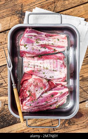 Gambi di agnello marinati con erbe, spezie e timo. Carne di montone pronta per la cottura. Sfondo di legno. Vista dall'alto. Foto Stock