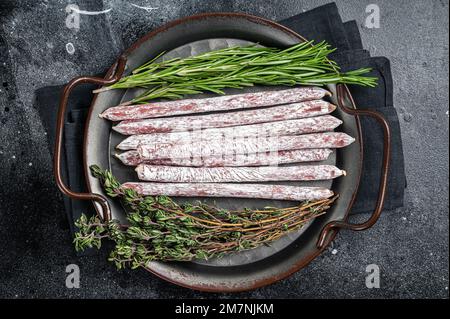 Tapa mini fuet salsiccia spagnola con erbe. Sfondo nero. Vista dall'alto Foto Stock