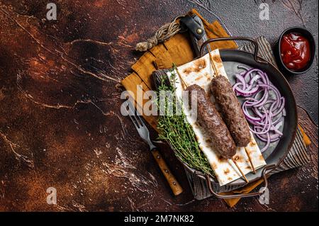 Adana Kebab turco da carne di agnello tritata su spiedino con focaccia e cipolla. Sfondo scuro. Vista dall'alto. Spazio di copia Foto Stock
