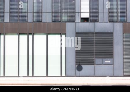 La disposizione delle persiane e degli elementi murali di un edificio forma un disegno grafico in bianco, marrone e grigio. Foto Stock