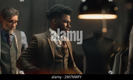 Giovane uomo d'affari afro-americano in vestito in elegante atelier designer di lusso o studio di sartoria. Abito da sposa o da lavoro su misura. Concetto di moda, artigianale, artigianale e couturier. Foto Stock