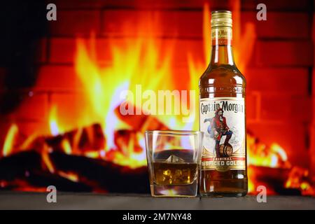 KIEV, UCRAINA - 4 MAGGIO 2022 Capitano Morgan bottiglia di alcol originale su tavolo di legno con camino rosso sullo sfondo. Produzione di alcool Elite Foto Stock