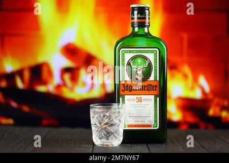 KIEV, UCRAINA - 4 MAGGIO 2022 Jagermeister bottiglia di alcol originale su tavolo di legno con camino rosso sullo sfondo. Produzione di alcool Elite Foto Stock