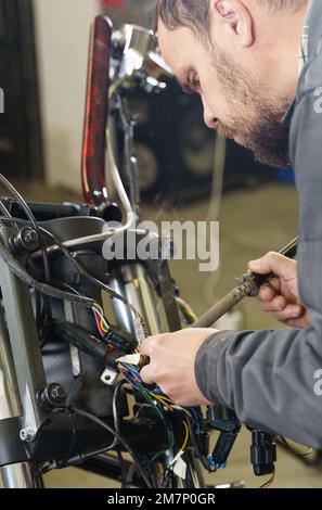 Un elettricista sta saldando i fili elettrici alle apparecchiature elettriche di una motocicletta. Primo piano. Concetto di trasporto Foto Stock