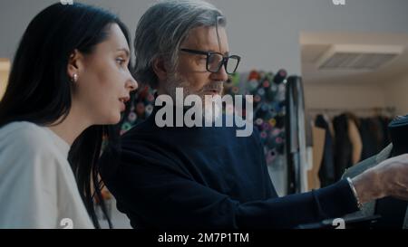 Uomo maturo fashion designer con tablet digitale parla con Seamstress della futura giacca e mostra il processo di sartoria sul manichino in atelier workshop. Concetto di moda e artigianato. Primo piano. Foto Stock