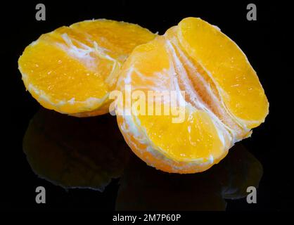 Spicchi di clementina agli agrumi su sfondo nero a specchio Foto Stock