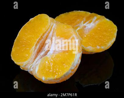 Spicchi di clementina agli agrumi su sfondo nero a specchio Foto Stock