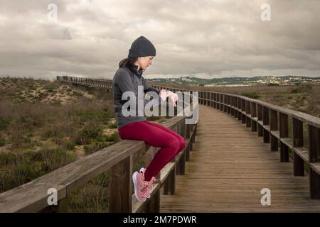 Runner femmina che riposa e controlla il suo orologio fitness tracker dopo aver corso su una passerella. Foto Stock