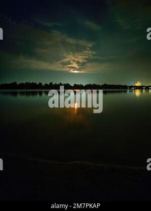Fotografia a colori della natura serale sul fiume. Luna piena che sorge sopra gli alberi. Bellissimo riflesso del sentiero lunare nell'acqua. Foto Stock