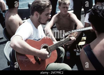 Gli equipaggi a bordo della portaerei USS MIDWAY (CV 41) suonano chitarre sul ponte di volo durante un periodo di attesa. Paese: Oceano Pacifico (POC) Foto Stock