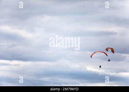 Immagine di alcuni parapendio che volano, contro un cielo grigio nuvoloso. Foto Stock