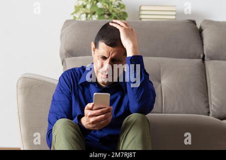 Unico Uomo triste controllo telefono cellulare seduta sul pavimento nel soggiorno di casa con uno sfondo scuro Foto Stock