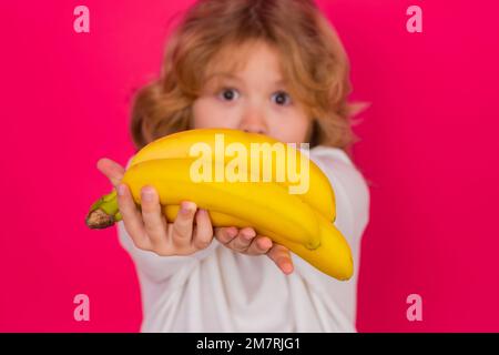 Bambino tenere banana in studio. Studio ritratto di carino ragazzo con banane isolato su sfondo rosso. Foto Stock