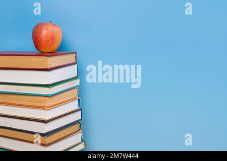 Pila di libri nella copertina colorata giaceva e libro con vecchie pagine e mela rossa su sfondo blu. Concetto di apprendimento per l'istruzione Foto Stock