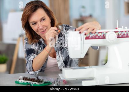 donna matura che ripara la macchina da cucire Foto Stock