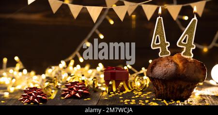 Numero 44 candele brucianti festive dorate in una torta, sfondo di festa in legno. quarantaquattro anni dalla data di nascita. il concetto di celebrare a b Foto Stock