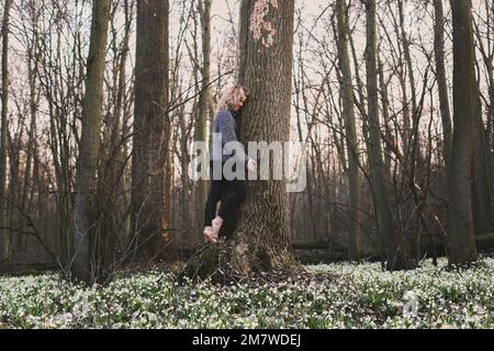 Donna bionda abbracciando grande albero tronco fotografia panoramica Foto Stock
