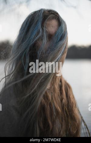 Primo piano lungo grigio marrone capelli nascondere il viso donna con vento ritratto immagine Foto Stock