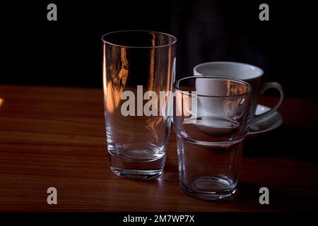 Bicchieri d'acqua e tazze da caffè in vetro trasparente posizionati su un tavolo di legno. Foto Stock