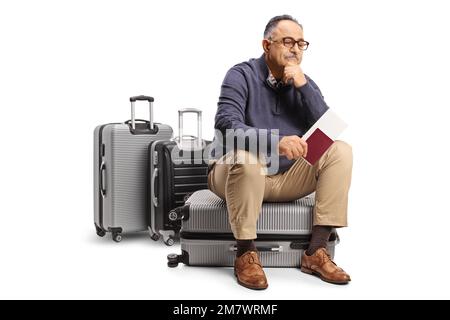 Uomo maturo penoso seduto su una valigia e in attesa con un passaporto in mano isolato su sfondo bianco Foto Stock