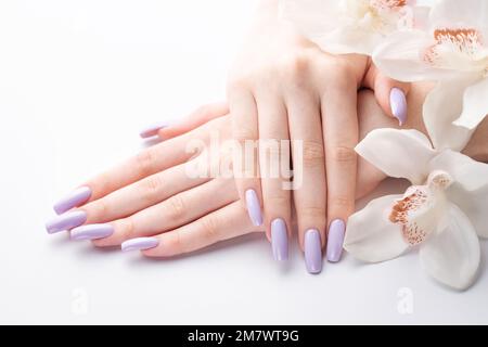 Mani di ragazza con delicata manicure viola e fiori di orchidea. Il concetto di bellezza e cura del corpo. Foto Stock