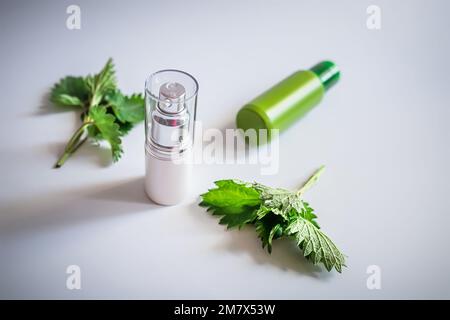 Crema corpo, o lozione con foglie di ortica in un contenitore di plastica su uno sfondo bianco con ombre alla moda. Foto Stock